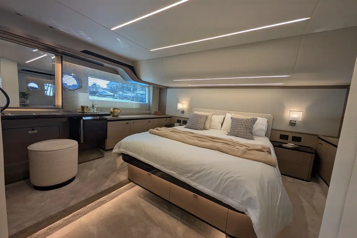 Luxurious yacht bedroom with a king-sized bed, textured pillows, ambient lighting, and a view through round windows.